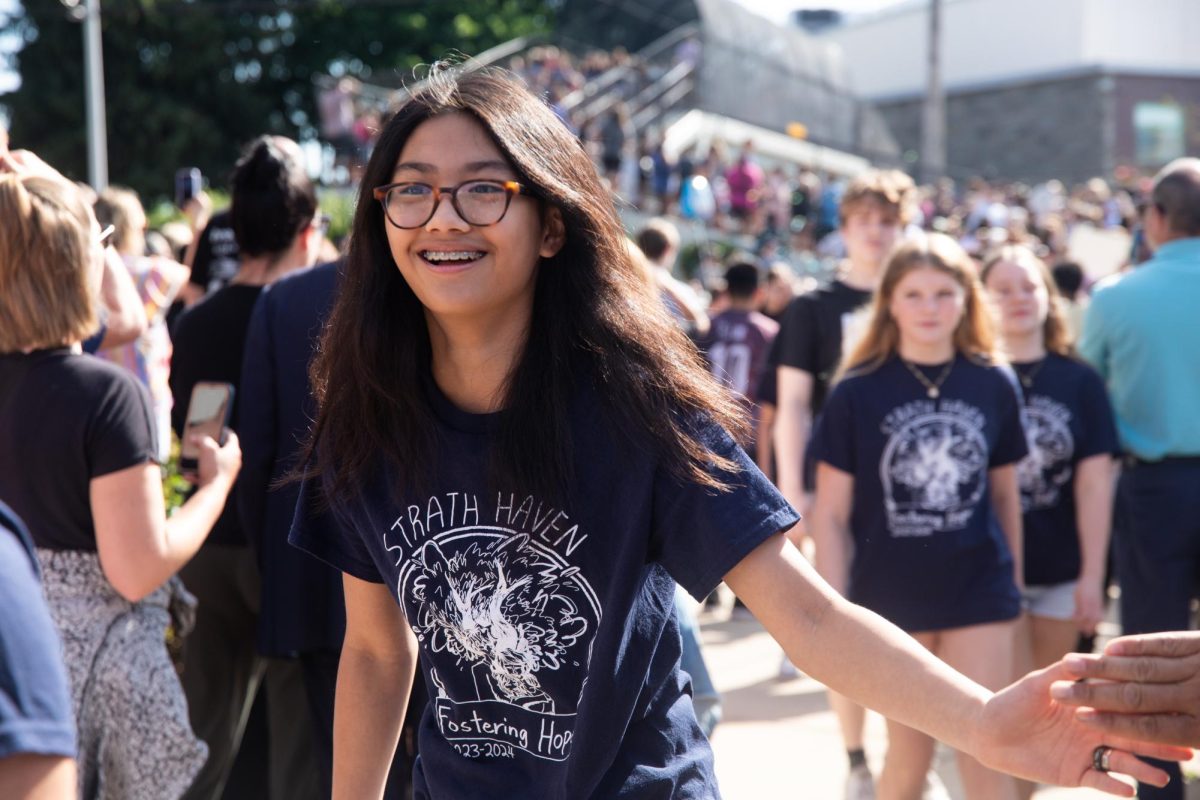 Rising freshman Kyubi Suico slaps one of her teachers' hands with a smile as she passes by to enter the high school building during the bridge crossing. 