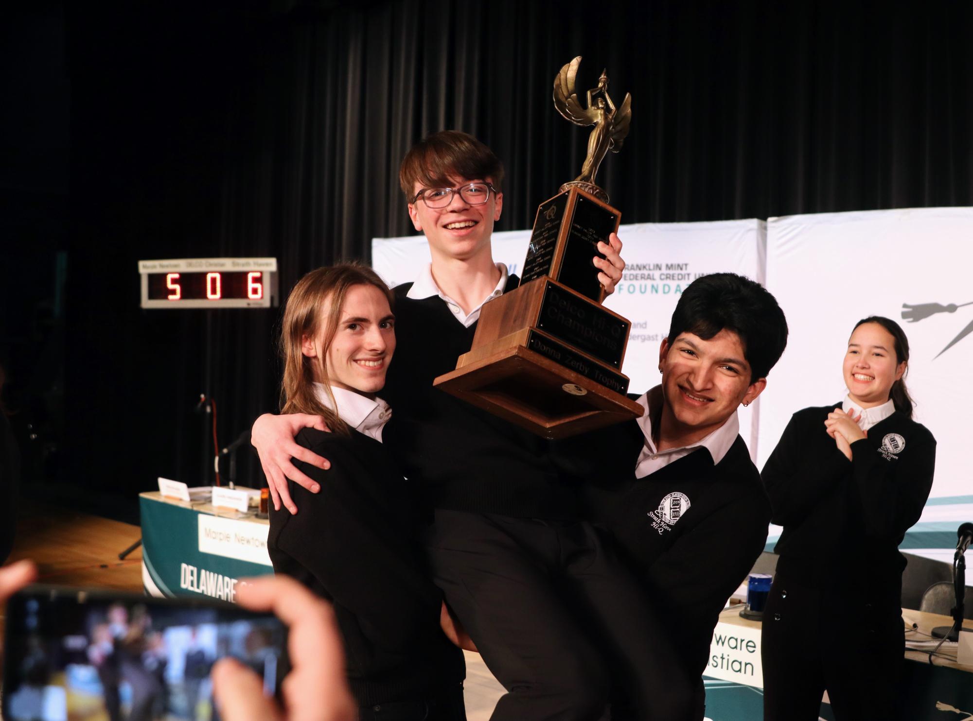 Seniors Sebastian Reed and Tanush Talekar hold sophomore Clark Kerkstra with the trophy after the match.