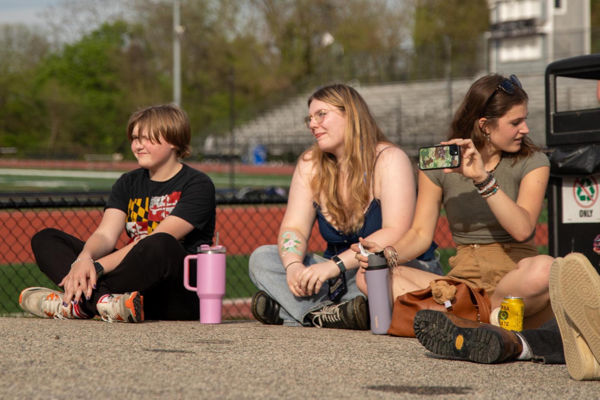 Freshman Luke Hanna and seniors Violet Abrahamsson and Paige Katsapis sit on the pavement to watch the live music performances at Spring Fling. 