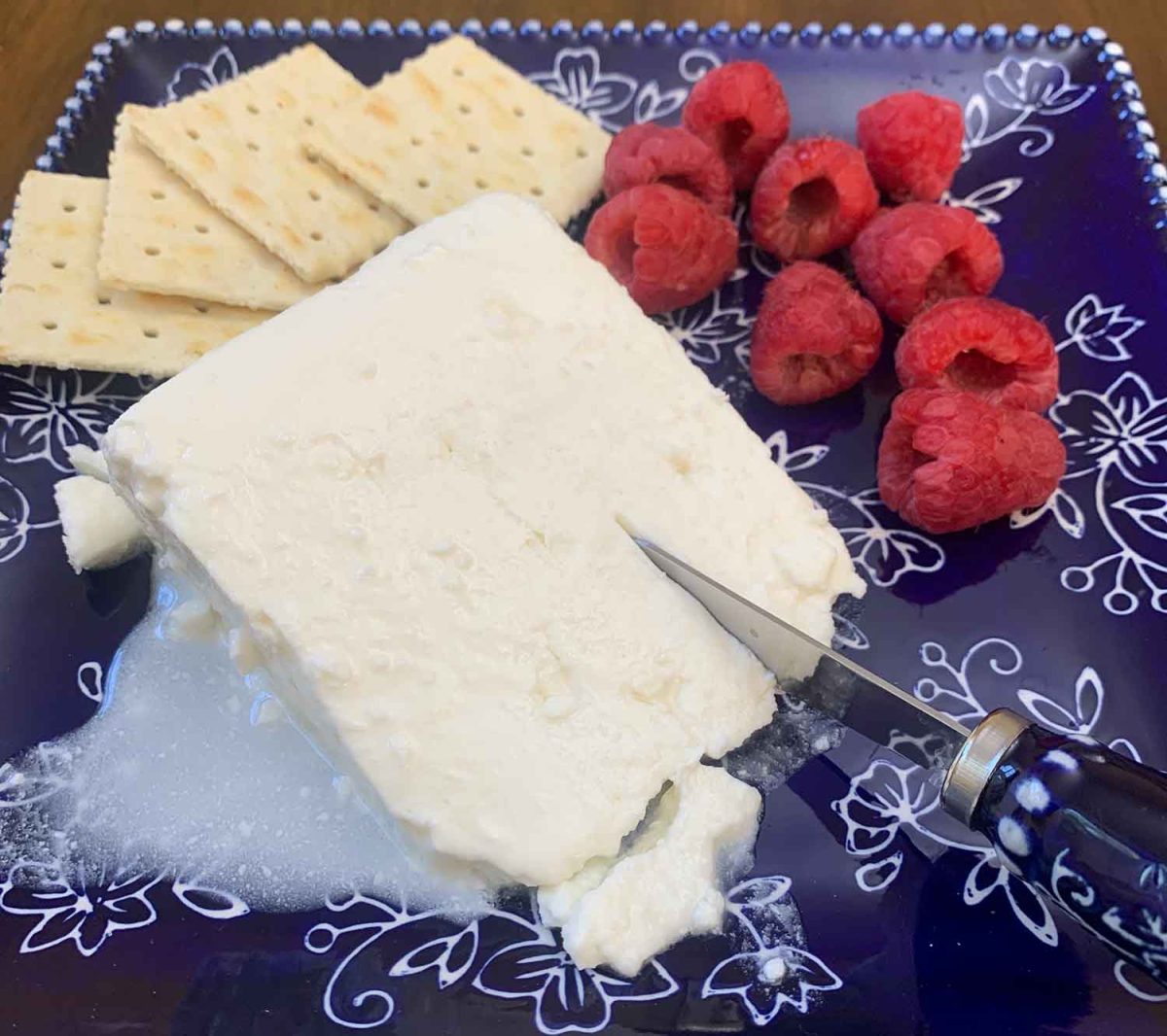 Feta being sliced with a side of crackers and raspberries.