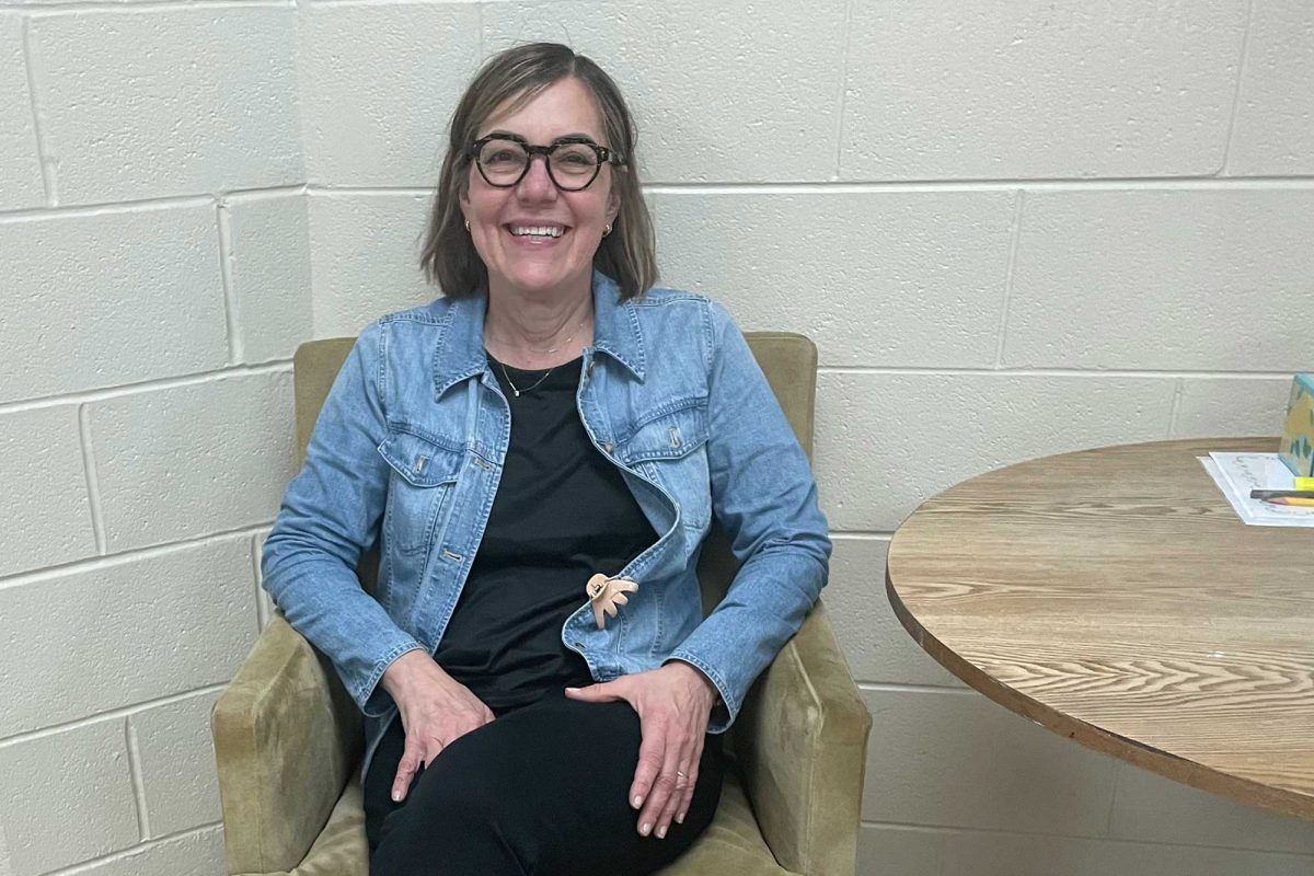 Ms. Paulette Slowik-Speaker smiles from an armchair in her classroom.