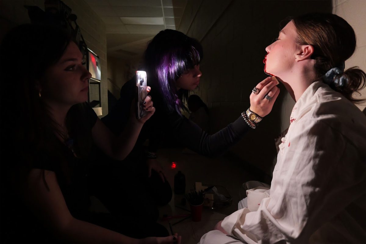 Madeline Beck (10) and Alice Rieger (10) work to transform Leah Reece (11) from formidable cook into gory murder-victim backstage on Nov 22. The performance of "Clue" included seven deaths, complete with fake blood and prop weapons.
