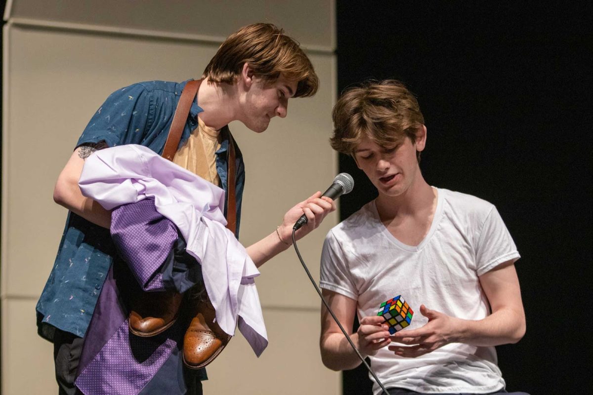 Ben Holtman '23 holds the mic and Archie Bracegirdle's '23 clothes while Bracegirdle adlibs and solves a Rubik's Cube. Bracegirdle's next act was to solve it while he held his breath underwater.