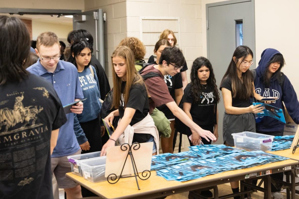 Seniors reach for signing booklets and pens before entering the cafeteria for Senior Breakfast on May 29. The booklet design connects to the 2026 yearbook theme of 'Lock In.'