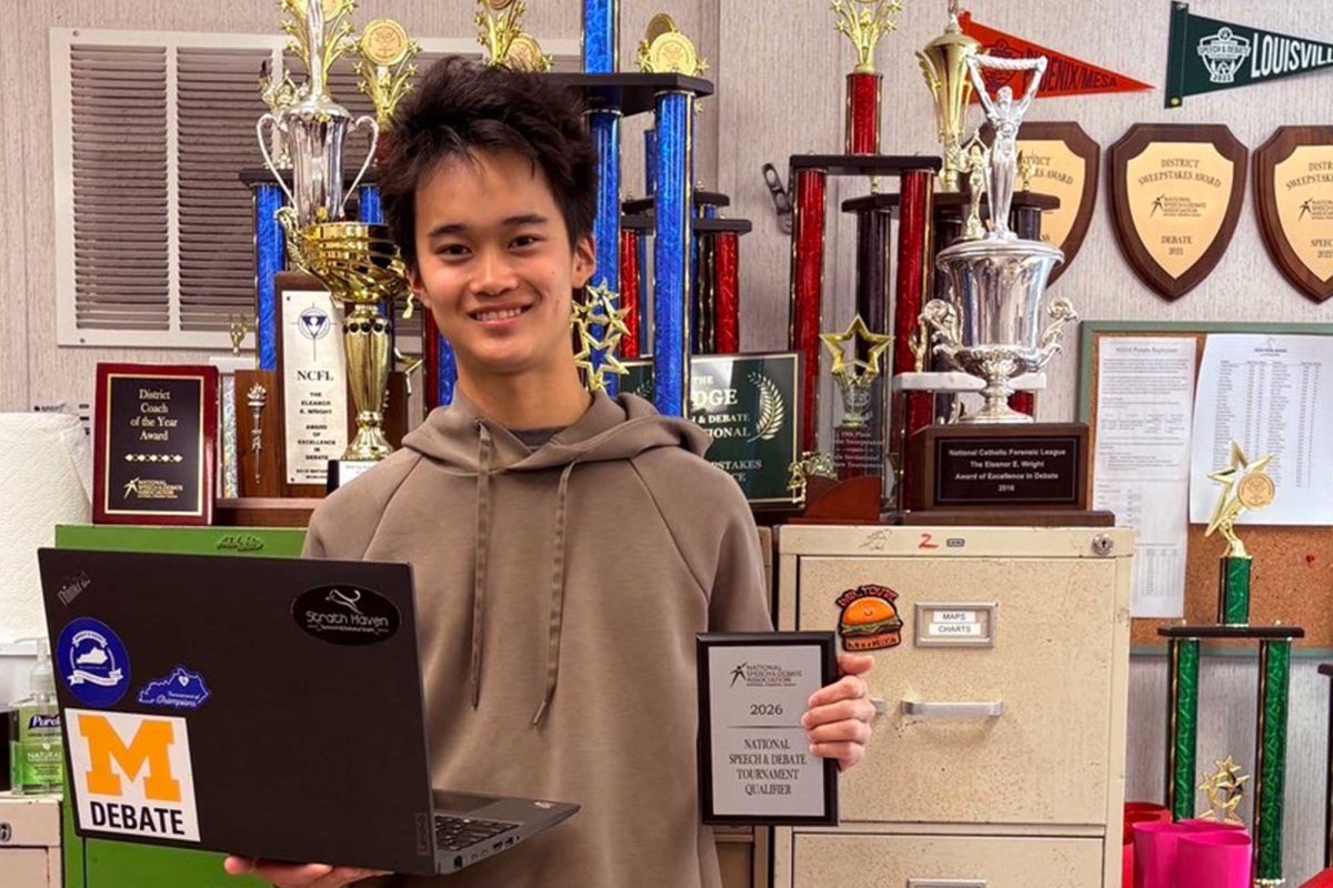 Vincent Zhu poses with his laptop and national qualifier plaque in front of the trophy display in Mr. Jeff Kahn's classroom.