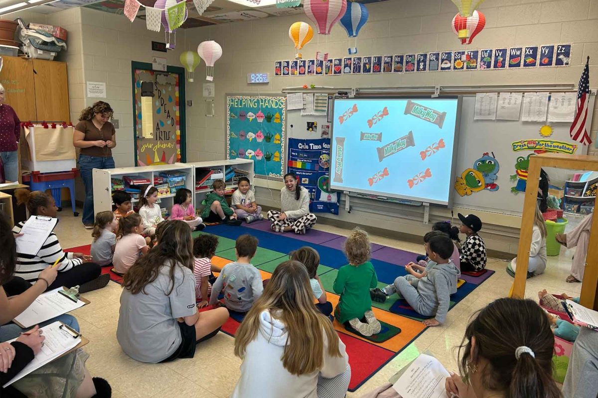 High schoolers and preschoolers gather around the carpet for circle time. This is one of the many activities that occurs in the preschool.